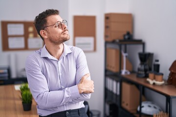 Young hispanic man at the office looking to the side with arms crossed convinced and confident