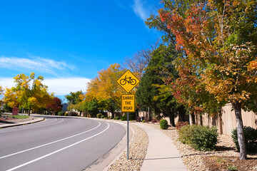 Yellow diamond warning road sign with bicycle symbol and 'Share the road' text along empty curved...