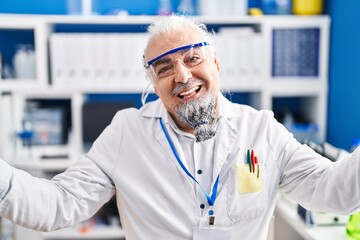 Middle age man with grey hair working at scientist laboratory celebrating achievement with happy smile and winner expression with raised hand