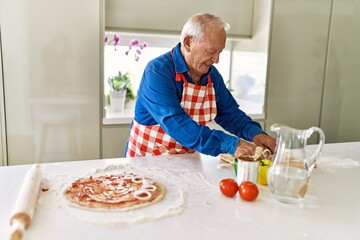 Senior man smiling confident cooking pizza at kitchen