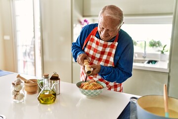 Senior man smiling confident pouring pepper on spaghetti at kitchen