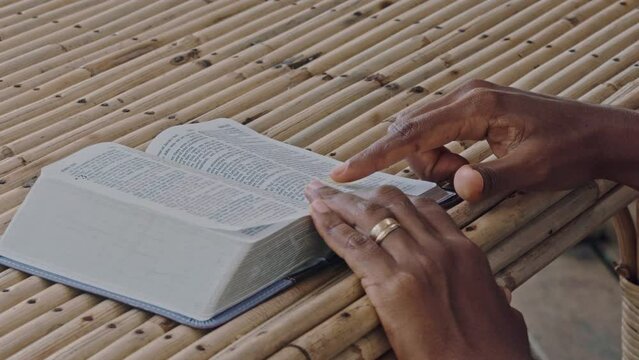 A open Bible on a table is read by someone with their fingers on its page.