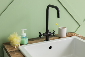 Fototapeta na wymiar Sink with bath accessories on table near green wall