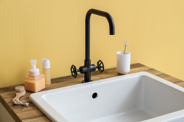 Fototapeta na wymiar Sink with bath accessories on table near yellow wall
