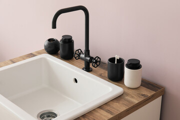 Sink with bath accessories on table near pink wall