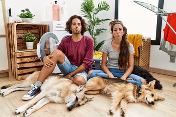 Young hispanic couple doing laundry with dogs looking at the camera blowing a kiss on air being lovely and sexy. love expression.