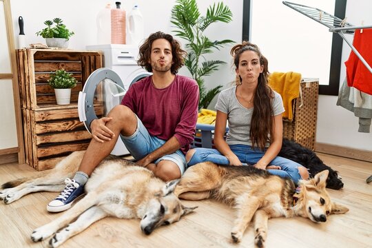 Young Hispanic Couple Doing Laundry With Dogs Looking At The Camera Blowing A Kiss On Air Being Lovely And Sexy. Love Expression.