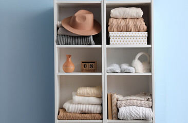 Shelving unit with sweaters, hat and decor near blue wall