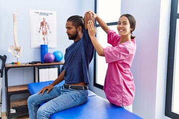 Man and woman wearing physiotherapist uniform having rehab session stretching arm at physiotherpy...