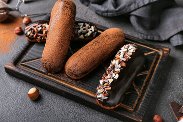 Wooden board with sweet chocolate eclairs on dark background, closeup
