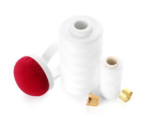 Thread spools, thimbles and pincushion on white background