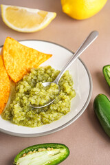 Plate of tasty green salsa sauce with nachos on color background, closeup