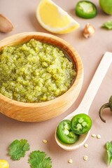 Wooden bowl of tasty green salsa sauce on color background, closeup