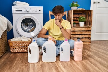 Arab man with beard doing laundry sitting on the floor with detergent bottle feeling unwell and...
