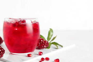 Glass of cold pomegranate juice on light background