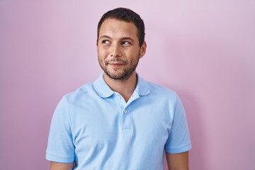 Hispanic man standing over pink background smiling looking to the side and staring away thinking.