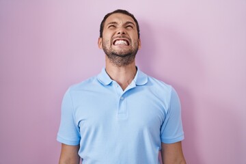 Hispanic man standing over pink background angry and mad screaming frustrated and furious, shouting with anger. rage and aggressive concept.