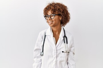 Young african american woman wearing doctor uniform and stethoscope looking away to side with smile...
