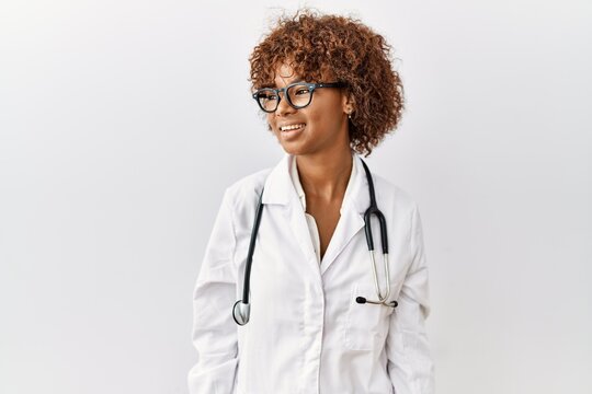 Young african american woman wearing doctor uniform and stethoscope looking away to side with smile on face, natural expression. laughing confident.