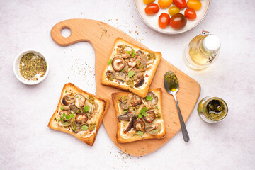 Wooden board of tasty toasts with cream cheese, mushrooms and pesto sauce on light background