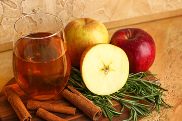 Wooden board with glass of fresh apple juice, fruits, rosemary and cinnamon sticks on table, closeup