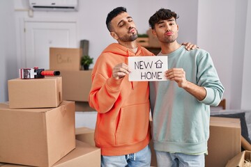 Young hispanic gay couple moving to a new home looking at the camera blowing a kiss being lovely...