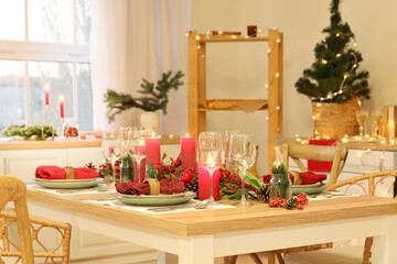 Christmas table setting with burning candles, fir cones and rowan in kitchen