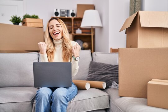 Young blonde woman using laptop with winner expression at new home