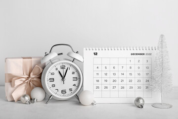 Flip calendar for December 2022, Christmas balls, alarm clock and gift on light background