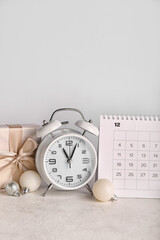 Flip calendar for December 2022, Christmas balls, alarm clock and gift on light background
