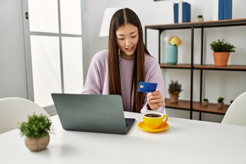 Fototapeta premium Young chinese girl buying using laptop and credit card sitting on the table at home.