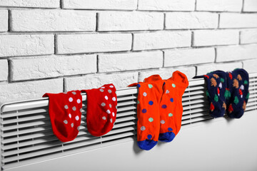 Warm socks drying on electric radiator near white brick wall