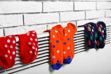 Warm socks drying on electric radiator near white brick wall, closeup