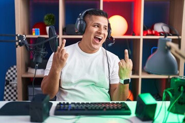 Young hispanic man playing video games showing middle finger doing fuck you bad expression, provocation and rude attitude. screaming excited