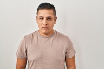 Hispanic young man standing over white background relaxed with serious expression on face. simple and natural looking at the camera.