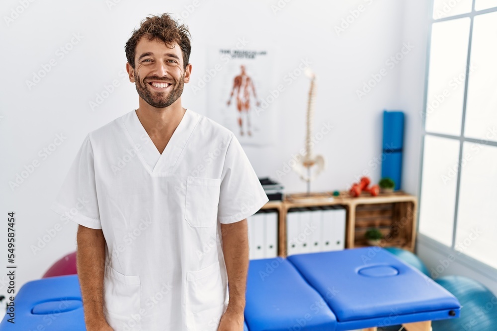 Sticker Young handsome physiotherapist man working at pain recovery clinic with a happy and cool smile on face. lucky person.