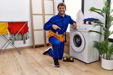 Young hispanic man working on washing machine smiling happy pointing with hand and finger