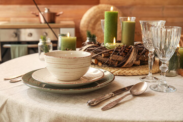 Christmas table setting with burning candles and wreath in kitchen, closeup