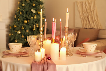 Christmas table setting with burning candles and balls in dining room