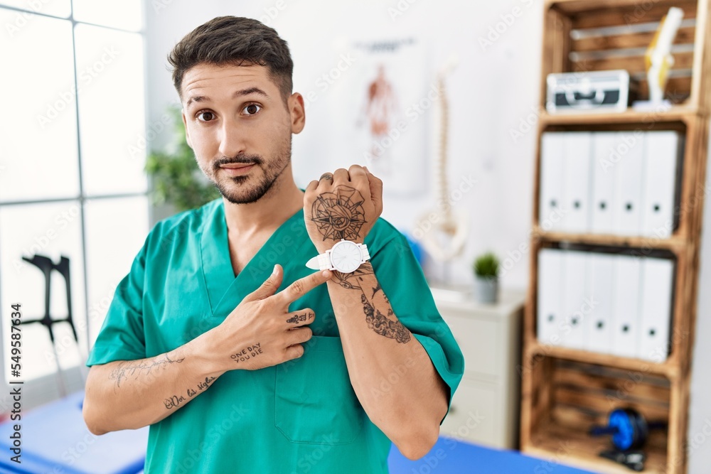 Canvas Prints young physiotherapist man working at pain recovery clinic in hurry pointing to watch time, impatienc