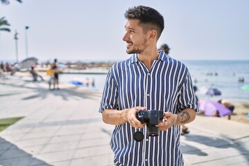 Young handsome man using dslr photography camera by the sea