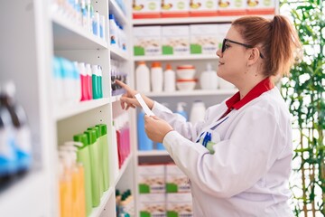 Young beautiful plus size woman pharmacist smiling confident reading prescription at pharmacy