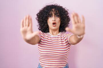 Young middle east woman standing over pink background doing stop gesture with hands palms, angry and frustration expression