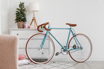 Bicycle near chest of drawers with Christmas tree and lamp in living room