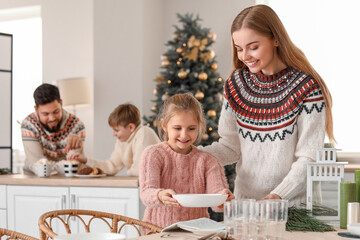 Little girl with her mother setting dining table in kitchen on Christmas eve