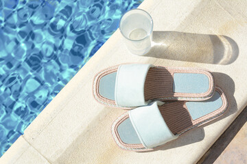 Stylish slippers and glass of water near outdoor swimming pool on sunny day, space for text