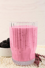 Glass of delicious blackberry smoothie, fresh berries and flowers on white wooden background