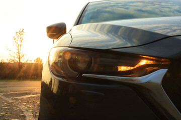Fototapeta na wymiar Black modern car parked on road at sunset, closeup of headlight