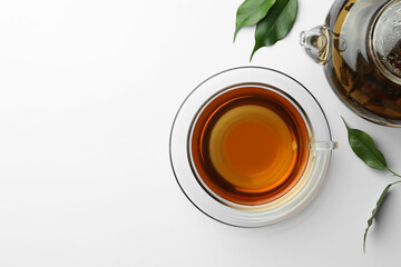 Fresh green tea in glass cup with saucer and leaves on white table, flat lay. Space for text