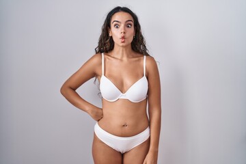 Fototapeta premium Young hispanic woman wearing white lingerie making fish face with lips, crazy and comical gesture. funny expression.